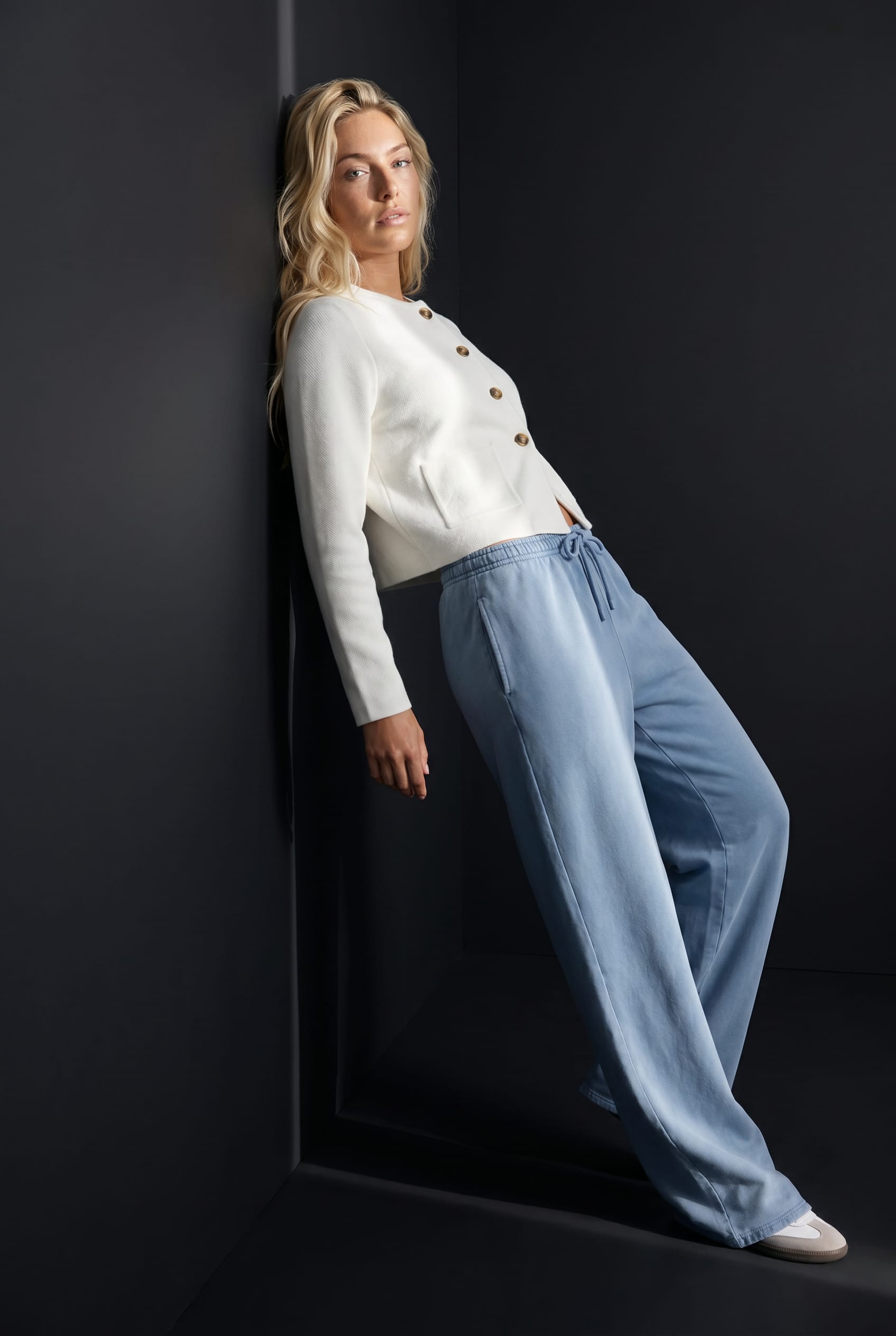 White cropped jacket and washed-blue trousers against the Noir Chrome wall